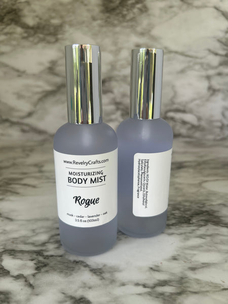 Two frosted gray bottles of Rogue Body Mist with shiny silver caps, displayed diagonally on a gray and white marble surface.