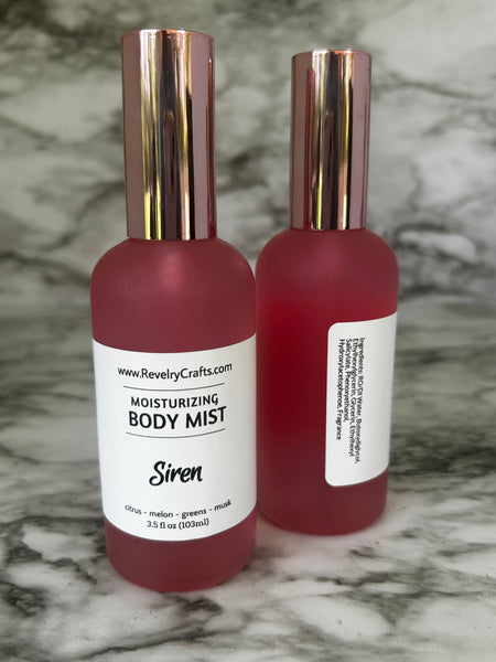 Two pink frosted glass bottles of Revelry Crafts Siren Moisturizing Body Mist with metallic rose gold caps, displayed on a gray and white marble surface.